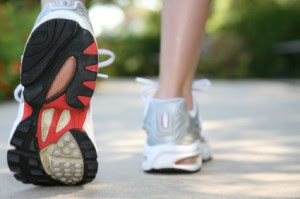 Close-up of a person walking on a path, wearing silver and white athletic shoes with red and black soles.